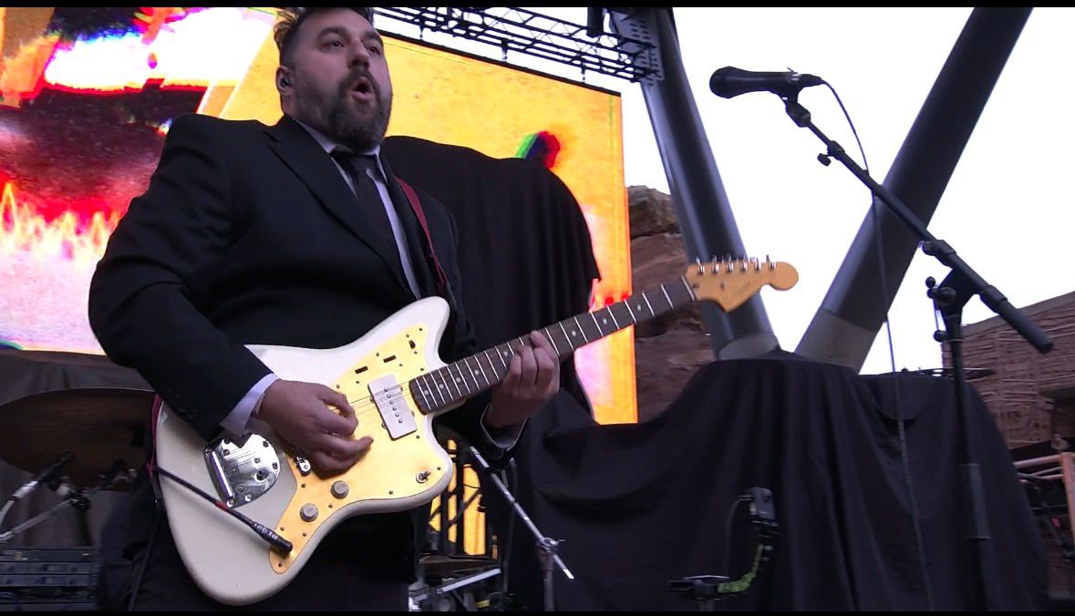 Guitarist performing at Red Rocks — white Jazzmaster guitar, LED screen in background