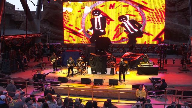 Codefendants full band performing at Red Rocks — LED screen showing animated stick figure motion system